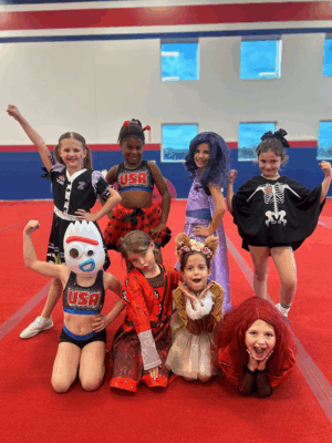 8 children in various Halloween costumes in a youth fitness facility